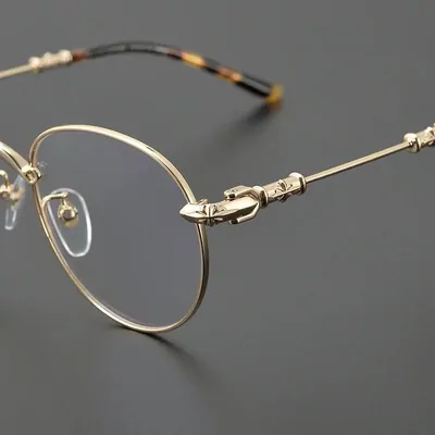 Round gold metal eyeglasses with tortoiseshell temple tips, on a grey background