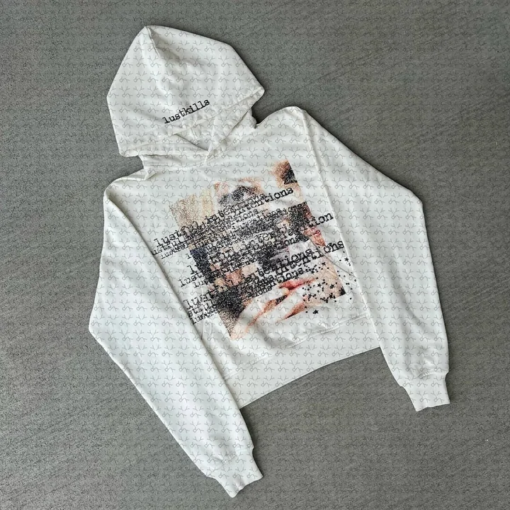 A light grey hoodie laid flat, printed across the chest with a collaged graphic and small blocks of text