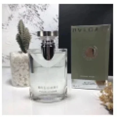 A clear glass flacon standing beside its boxed carton on a pale shelf with dried grass